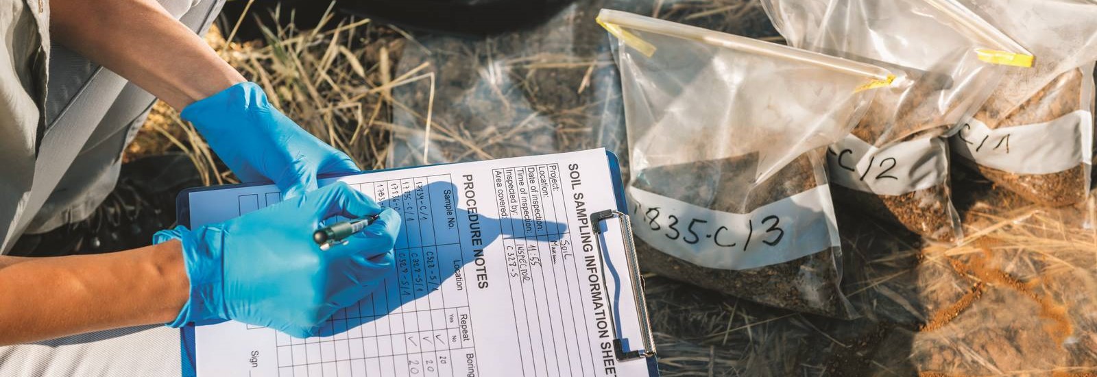 Low Section Of Agronomist Writing In Paper While Crouching On Field